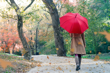 woman with red umbrella walking at the rain in beautiful autumn park