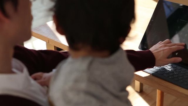 Father sitting with baby son in front of digital tablet