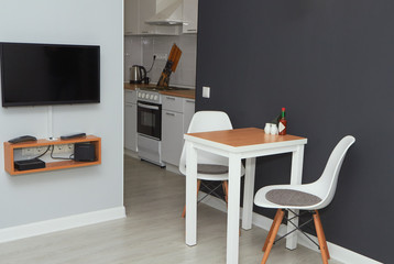 Design interior of the living studio room with small kitchen. White table and chairs in the foreground.
