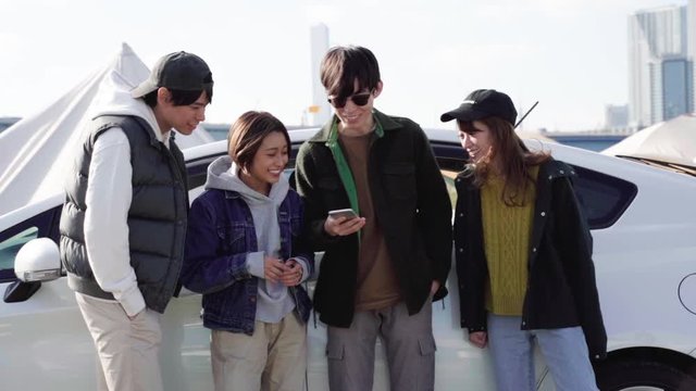 Group of young friends looking at smartphone outside car