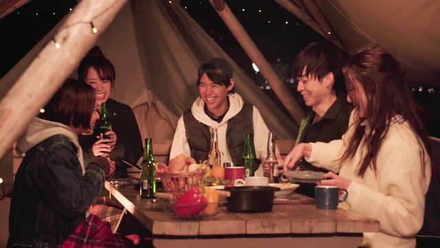 Group of friends sitting at table with food while camping at night