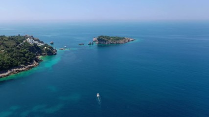 Aerial shot, quadcopter flies along the rocky seashore, where you can see the houses in some places, to a small island in the sea. The sea water is turquoise, clean and clear