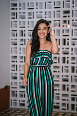 Portrait head shot of a young, attractive, beautiful and stylish Indian Asian woman in a green striped jumpsuit. She is smiling happily as she poses for her portrait in a stylish interior.