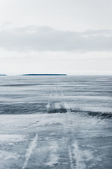 Winter landscape. A view of the frozen snow-covered lake. Forest in the background. Stormy evening clouds. Onega lake, Karelia, Russia