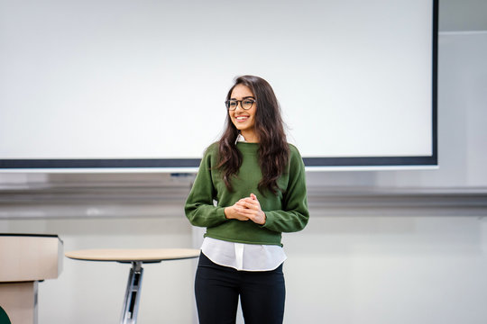 Portrait of a young, beautiful, attractive and intelligent-looking Indian Asian woman wearing spectacles in a sweater giving a business presentation to an audience.