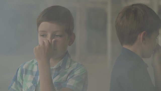 Two confused scared boys standing in the smoky room closing their noses with hands. Concept of danger. Fire, flammability, non-compliance with safety rules
