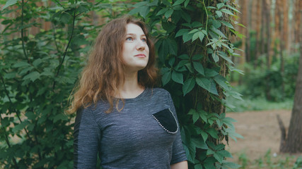 Satisfied woman looking dreamily standing in green Park. woman posing in the woods