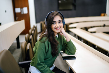 Portrait of a young, beautiful and attractive Indian Asian woman student in a preppy outfit sitting...