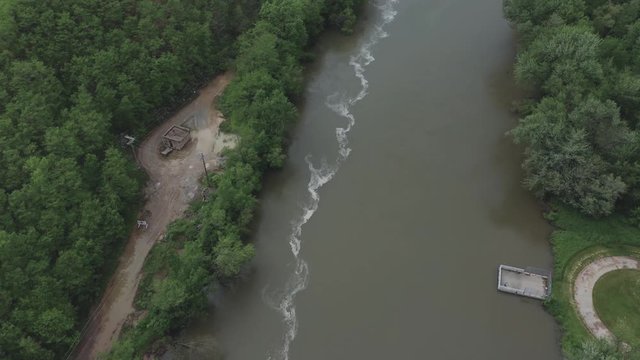 Drone flies over a river in the Midwestern USA and pans up to eventually reveal a quarry.  in summer, in 4K.