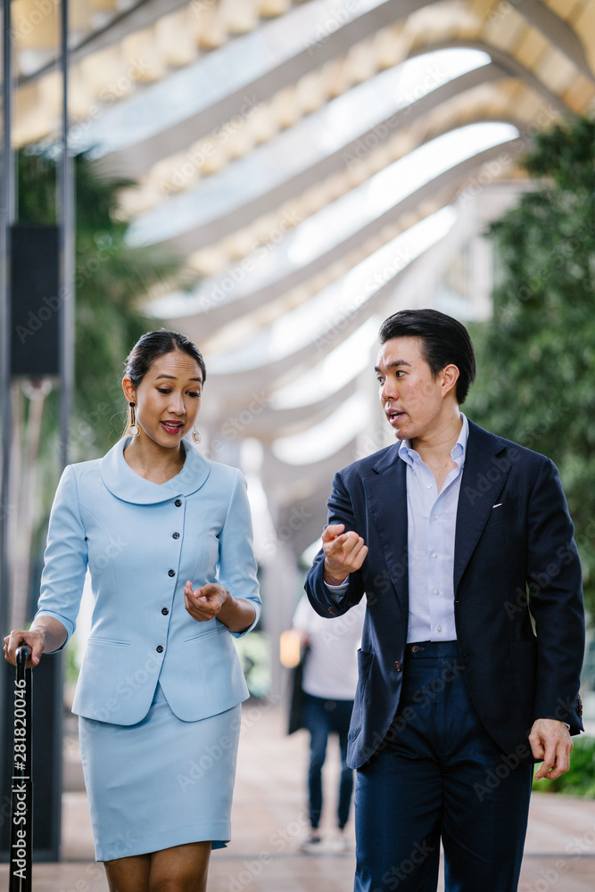 Wall mural portrait of two well-dressed and professional asian business people walking together in a modern cit