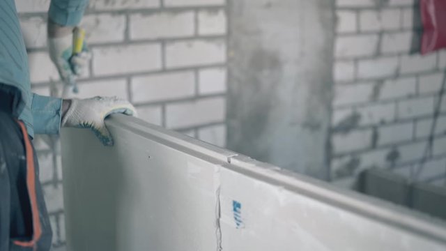 professional plasterer prepares gypsum plasterboard decorative wall and beats construction with rubber hammer closeup