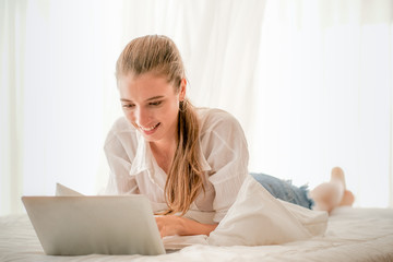 Obraz premium Beautiful girl with white shirt use laptop on bed to chat with someone and look happy.