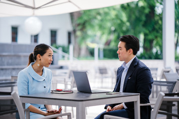 A Chinese Asian manager in a suit has a meeting with his colleague, a woman in a pale blue suit. He...