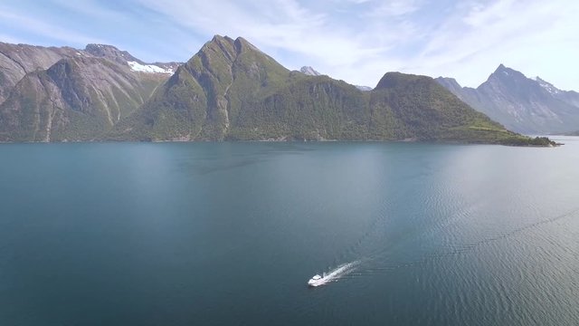 drone flying close to ocean/fjord, and driving fto the left, panning left, and showing a boat that is moving across the fjord.