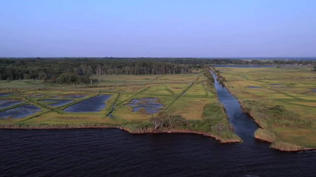 a slow aerial pan right at East Islip Marina & Park over the water looking up the long channel of the marsh area at sunset