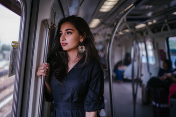Fototapeta na wymiar Portrait of a tall, slim, elegant and beautiful Indian Asian woman taking the train alone. She is leaning near the window and watching the scenery go by. The train is modern and clean.