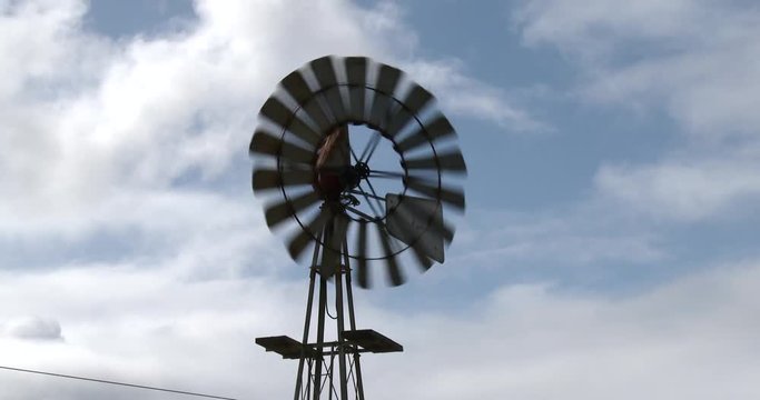 Close up of a wind pumps blades rotating with a background of moving clouds