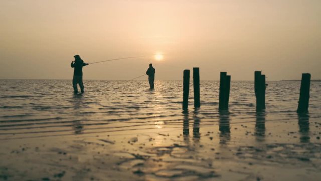 Two men fishing in the water with sunrise in the bagground and fog