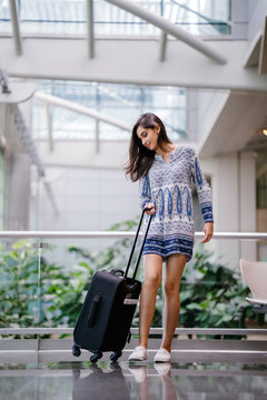 Portrait of a beautiful, attractive and young Indian Asian girl unzipping her bag to find something in her luggage or to repack her items before check in at the airport during the day.