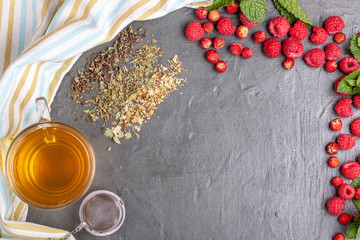 Cup of green tea with dry tea leaves on black concrete background with wild strawberries and raspberries
