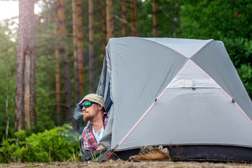 Naklejka na ściany i meble man in a hat and sunglasses lying in a tent and smoking a cigarette. concept of travel and camping