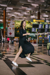 Portrait of an attractive, young and athletic north Indian Asian woman smiling and laughing as she leaps and jumps indoors in a mall or airport. She is wearing a casual black flowing dress.