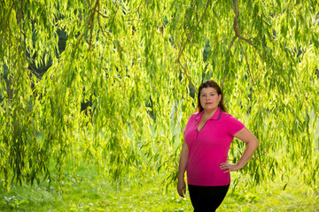 Lady poses for a portrait in the shade of a tree. She is serious and looking to the camera.