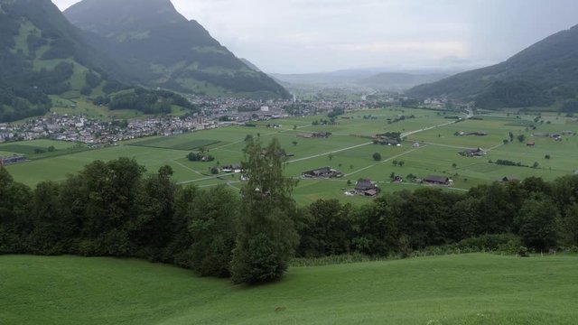 Perspective view of the Linth rivers valley surrounded by alpine montains near Glarus Nord in Switzerland. Scenic shot taken from hill-side on a cloudy day with the valley and mountains in foreground.