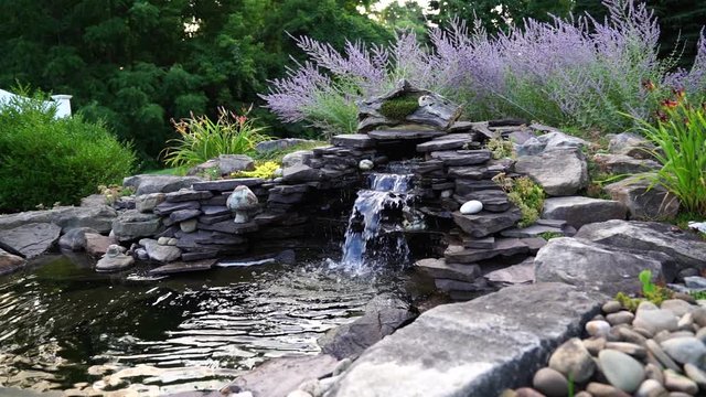 This is a HD  video of a garden waterfall filmed during the Golden Hour in July. It shows water flowing in a garden pond