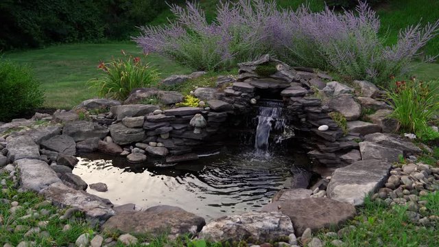 This is a UHD  video of a garden waterfall filmed during the Golden Hour in July. It shows water flowing in a garden pond.