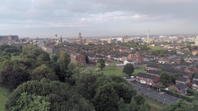 Liverpool city skyline cathedrals & radio city tower on waterfront distant aerial view. Pull back descent over park trees.