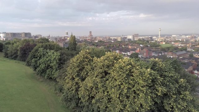 Liverpool city skyline cathedrals & radio city tower on waterfront distant aerial view. Reveal over tops of park trees to city view.