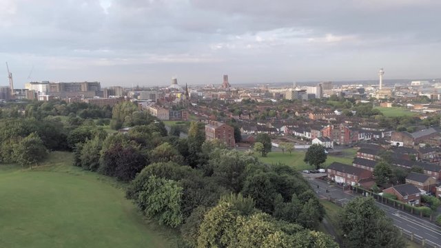 Liverpool city skyline cathedrals & radio city tower on waterfront distant aerial view. Descending over park trees.