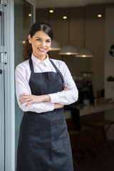 Beautiful waitress in apron smiling, showing welcome to coffee shop