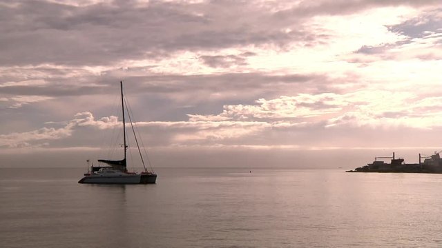 Lonely Sailboat Anchored in Calm Sea Water Near Pier Under Sunset Sunlight