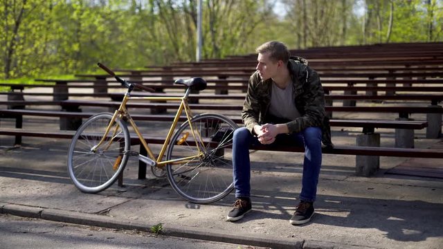 A young man sitting on a bench in a bleachers next to a yellow bicycle