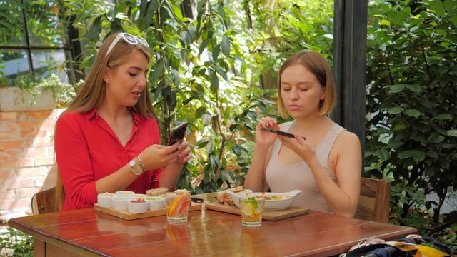Two young women friends eat breakfast together take phone food photo of dishes for social media