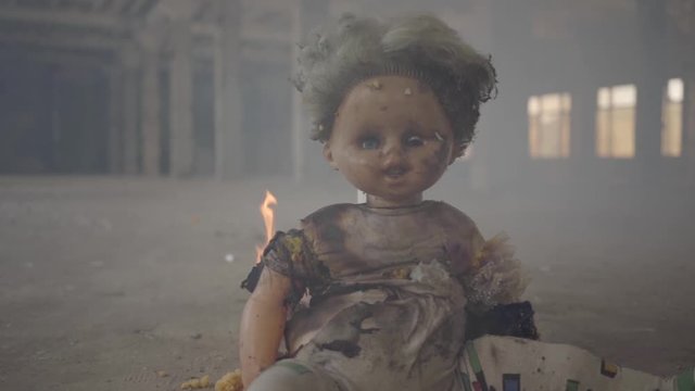 Scary doll burning on the floor in an abandoned smoky building. Concept of fire, flammability, non-compliance with safety rules.