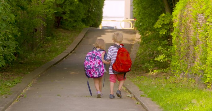 Two kindergarten students walking along a path to school together holding hands