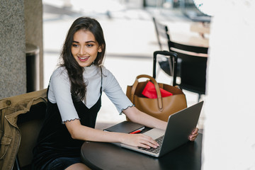 Portrait of young attractive profession Indian woman sitting at her desk and typing on her laptop. She appears to be smart yet relaxed.