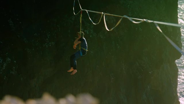 Bright handheld zooming shot of a caucasian male pulling himself back up on a slackline strung up over the ocean
