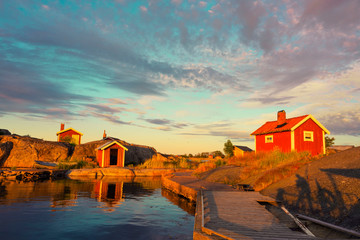Traditional red wooden house in the island with bridge on the water at sunset clouds sky in Sweden