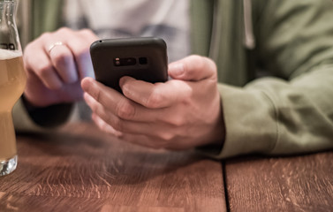 close up of man hand hold smartphone, drinking beer and reading message at bar or pub