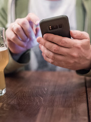 close up of man hand hold smartphone, drinking beer and reading message at bar or pub