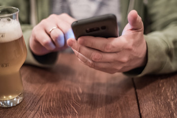 close up of man hand hold smartphone, drinking beer and reading message at bar or pub