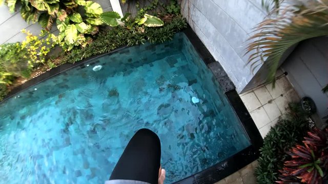 Slow Motion POV Shot of a man jumping off of a balcony and into a swimming pool below.
