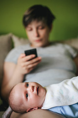 Disinterested mother playing with smartphone while guarding a small baby