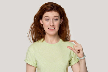 Headshot studio portrait confused girl showing with fingers something small