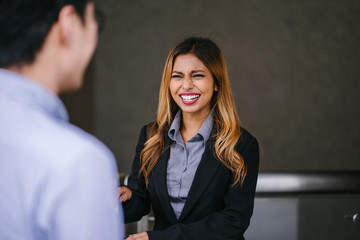 An office lady is telling a story to his colleague. She looks very attractive in her corporate attire.