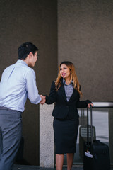 A young, tanned, beautiful and confident Asian business woman in a business suit smiles and shakes hand in agreement to mark a deal with an Asian man. They are standing in an Asia city during the day.